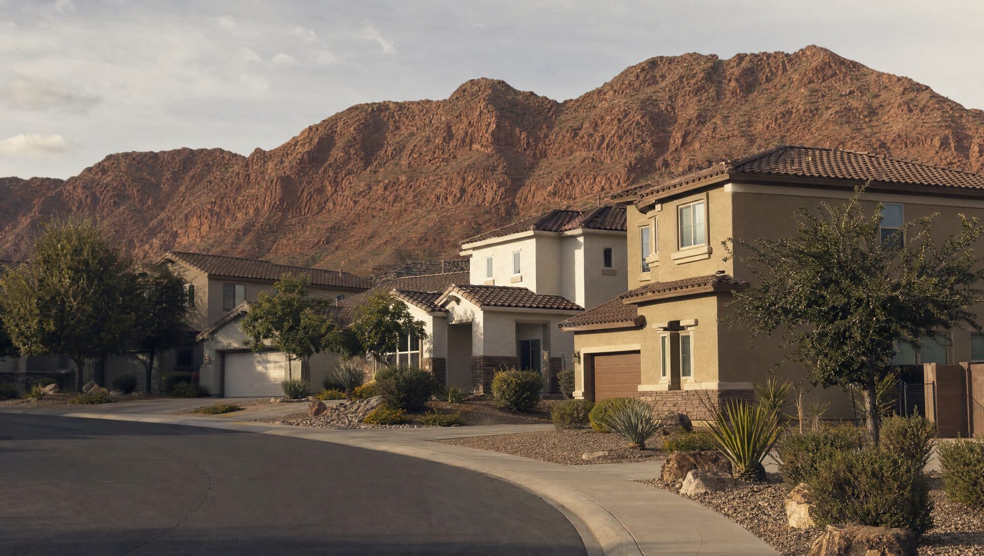 Two-story stucco homes on a curved street with red rocky hills behind