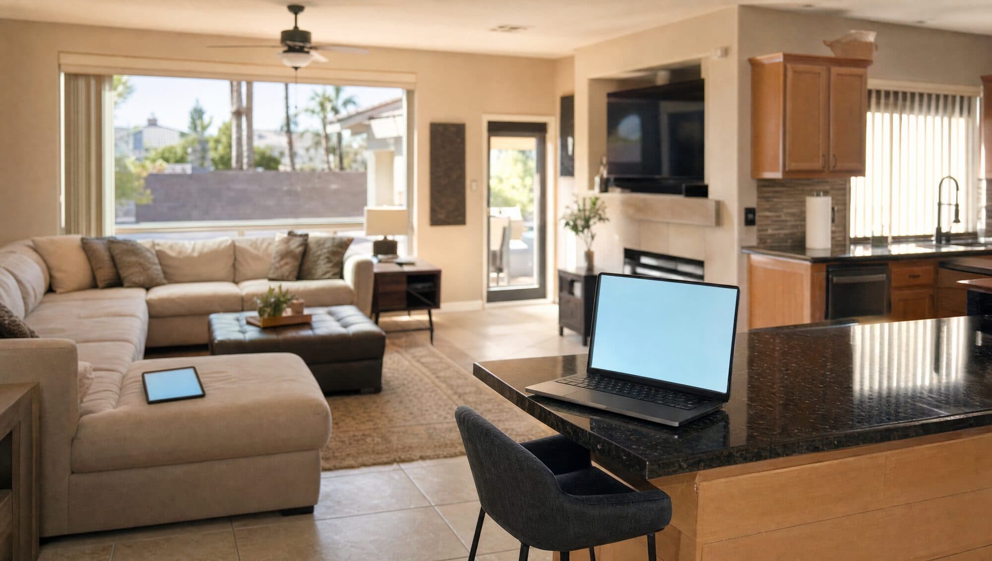 An open-plan living room and kitchen with a laptop on the island and a tablet on the sofa